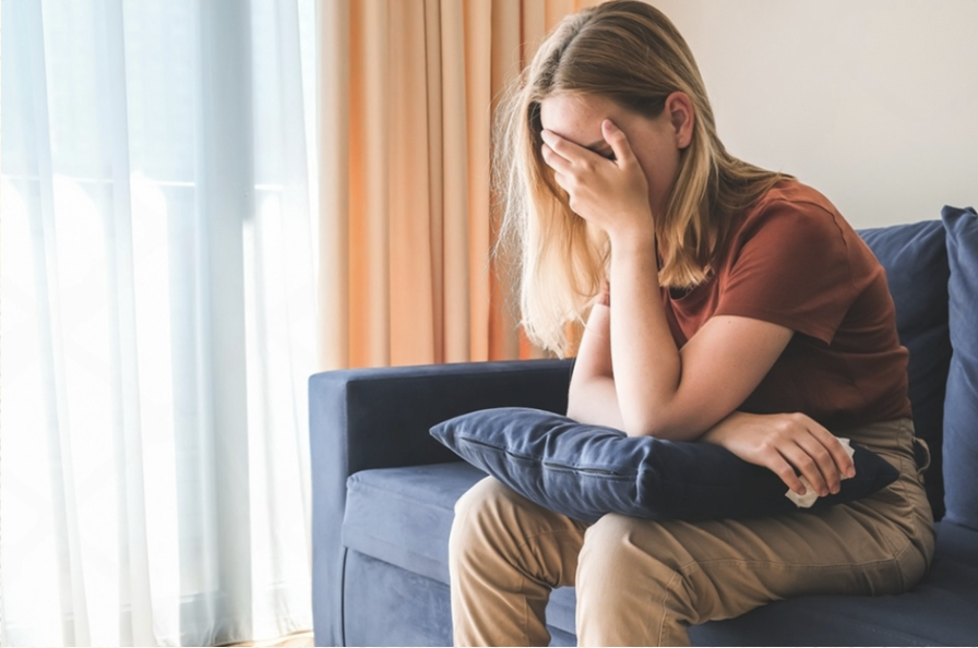 Woman sitting in an armchair with her hand over her face, experiencing anxiety