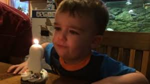 Young child watching a lit candle at a table