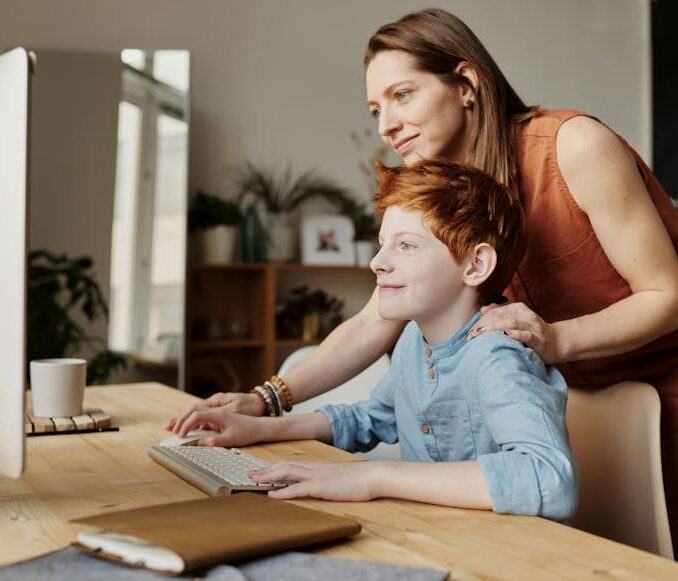 A mother and her child smiling while using a computer at home, focused on learning.