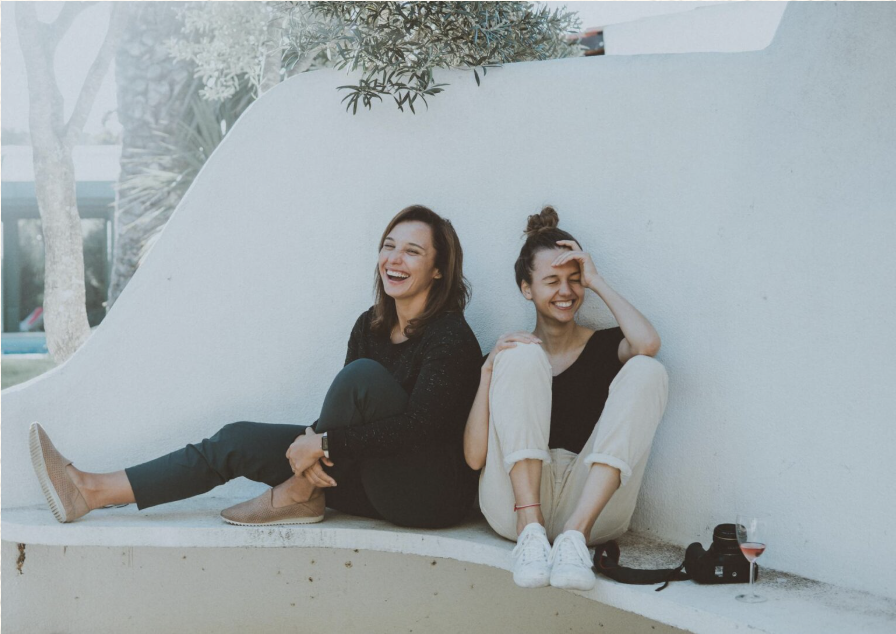 Two people sitting together on the floor against a white wall, relaxed and smiling