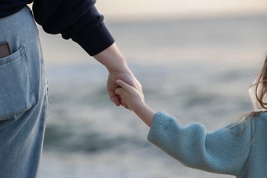 An adult and child holding hands by the water